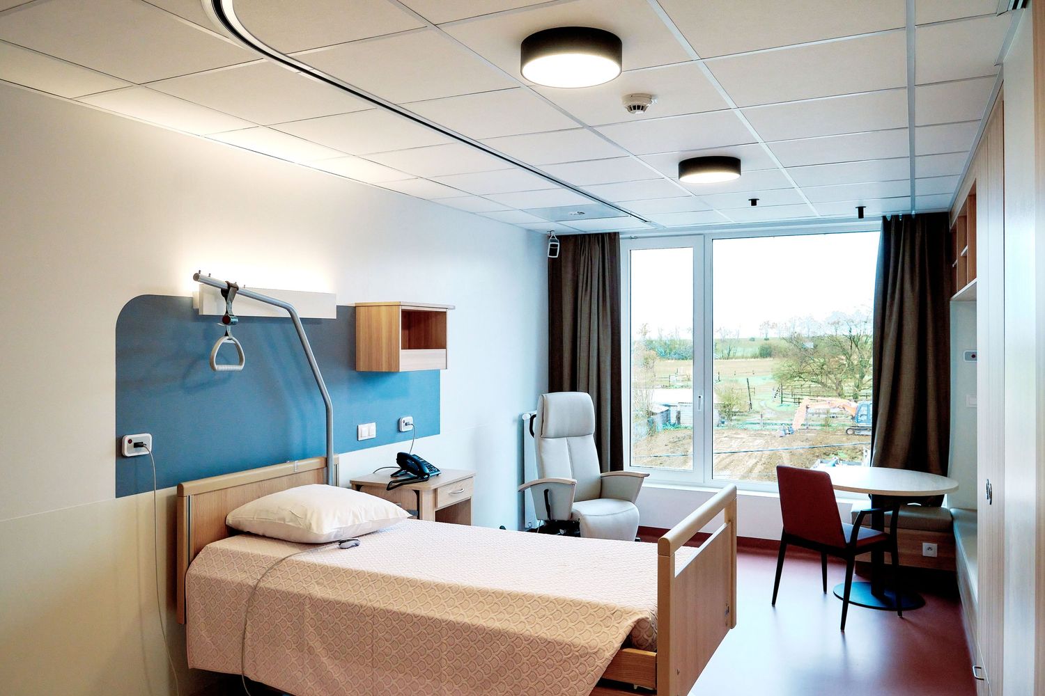 Panoramic view of a modern hospital patient room with large windows and medical equipment.
