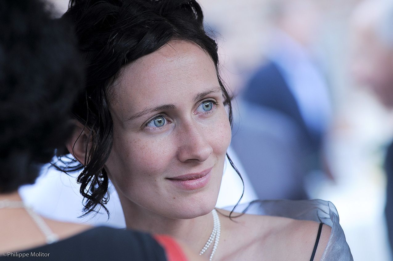 An elegant woman with dark hair and blue eyes wearing pearl necklace at a formal event.