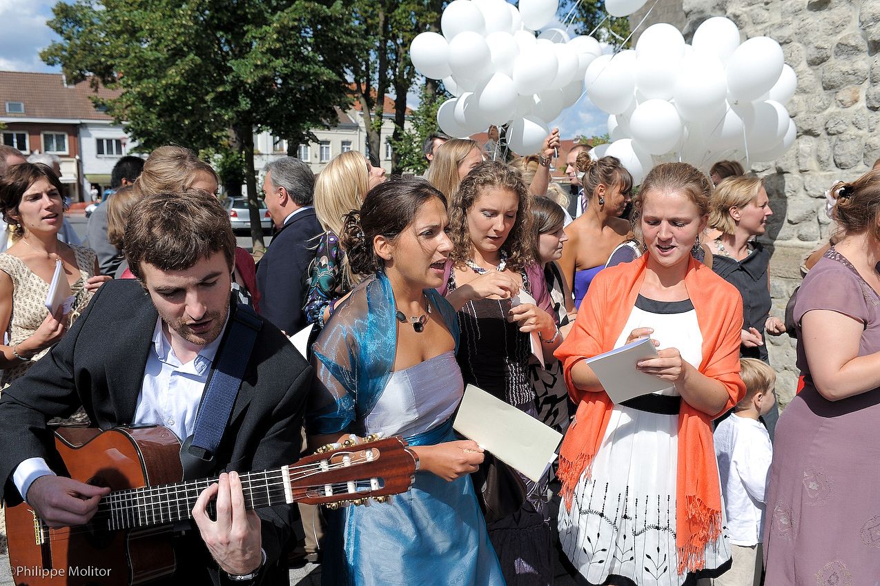 Outdoor gathering with musician playing guitar, people singing, and white balloons at a sunny celebration event.