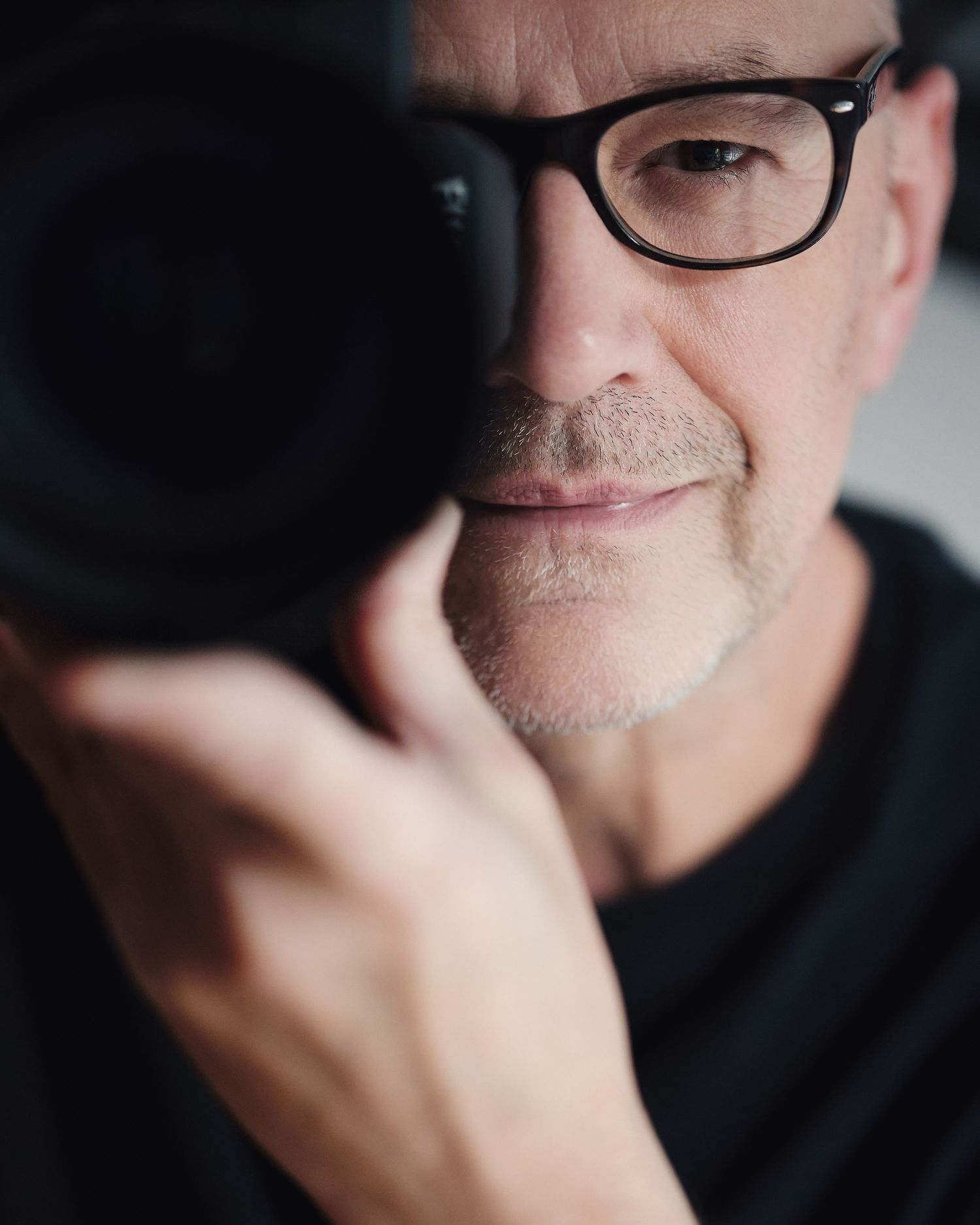 Middle-aged man with glasses holding a camera up to his eye, capturing a photo in a close-up portrait shot.