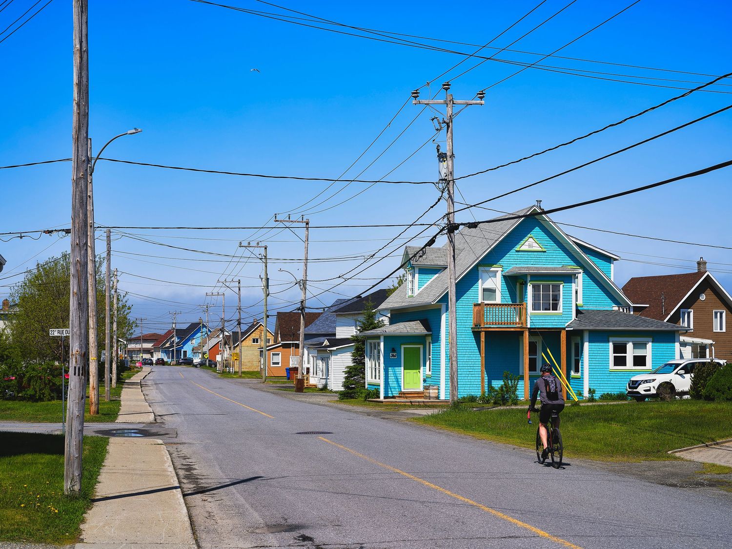 Row of colorful coastal houses with power lines along a rural road in a seaside village.