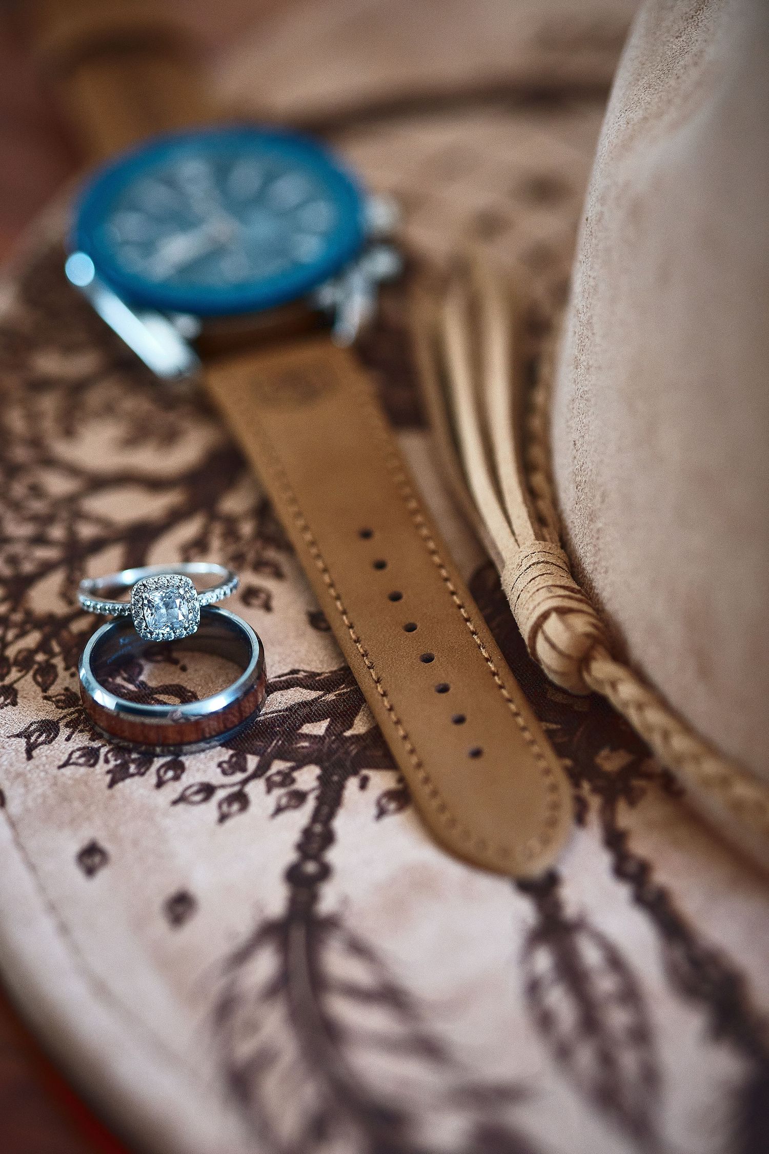 Wedding rings, blue watch, and cowboy hat on engraved wooden tray with feather design.