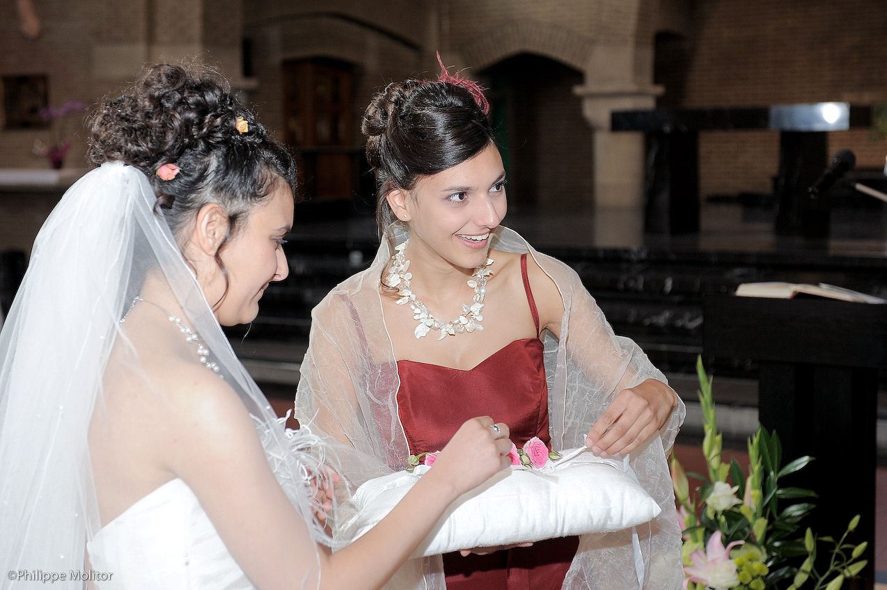 Bride and bridesmaid smiling together during wedding ring ceremony inside a church.