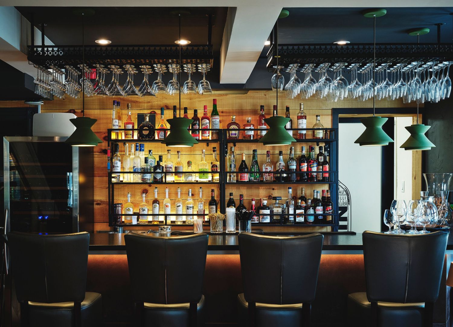 Well-stocked bar area with hanging wine glasses and illuminated bottle display.