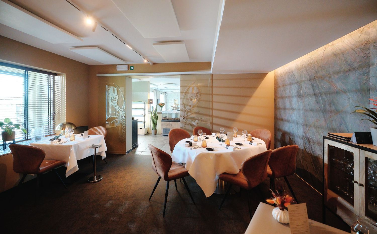 Modern restaurant dining room with clean lines, white tablecloths, and natural light streaming through windows.