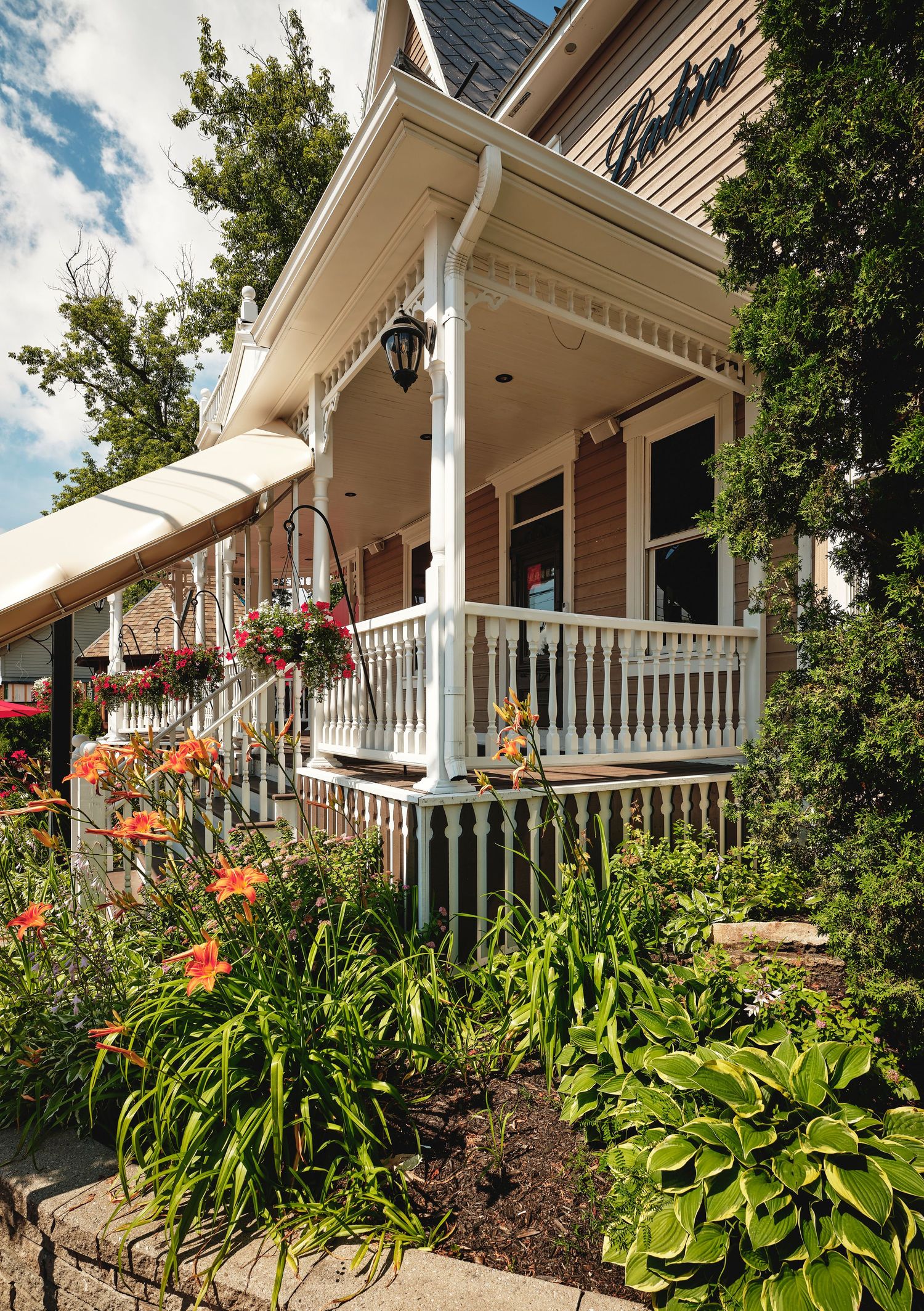 White porch of a Victorian restaurant with lush garden landscaping and hostas.