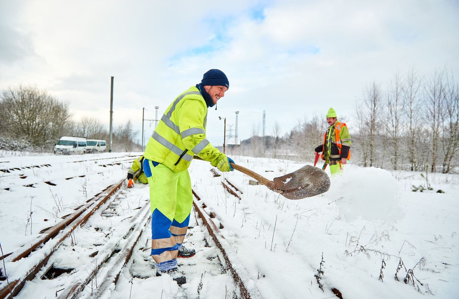 Railway maintenance worker in safety gear shovels snow from train tracks.