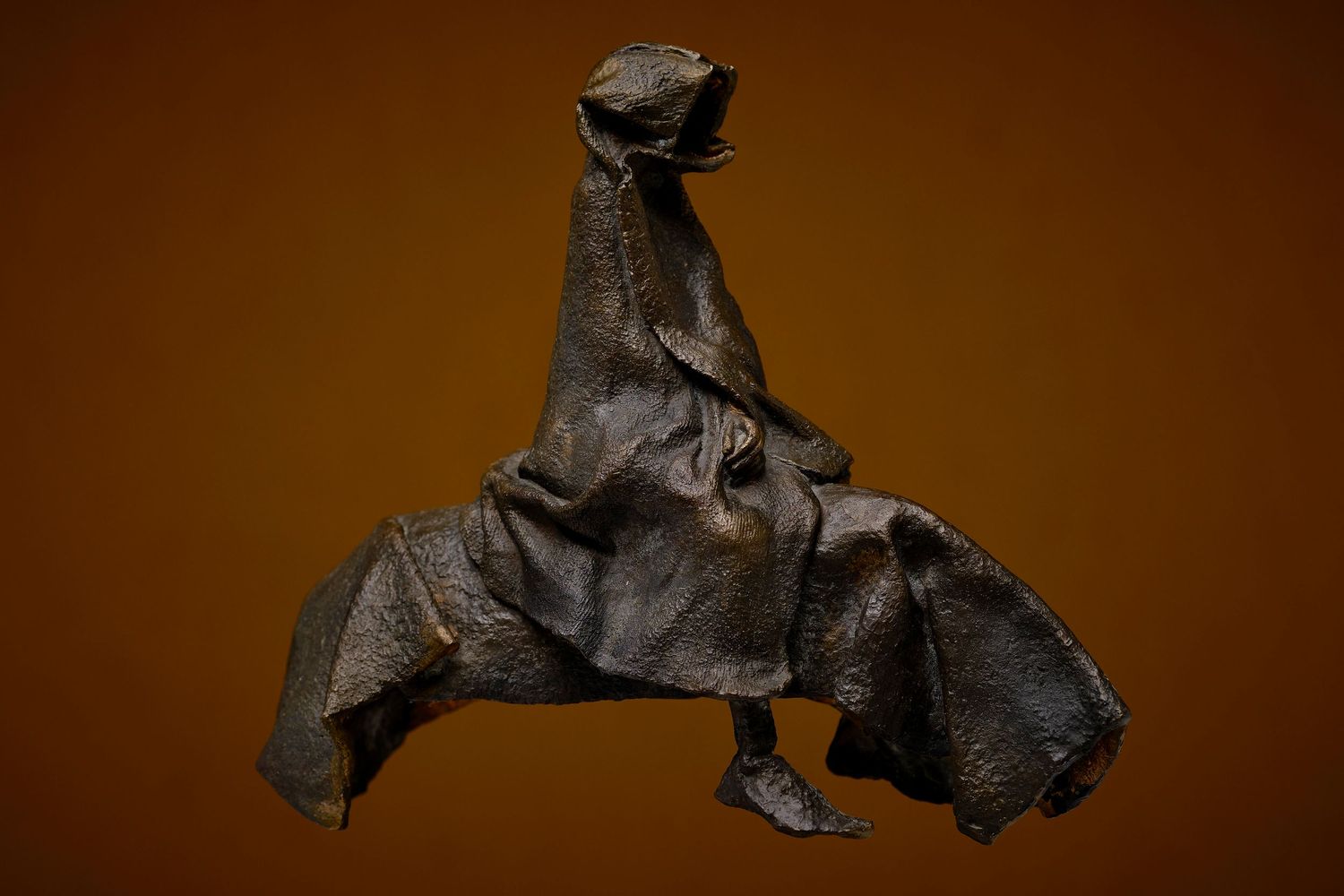 Dark abstract metal sculptures arranged in a series against a warm brown background.