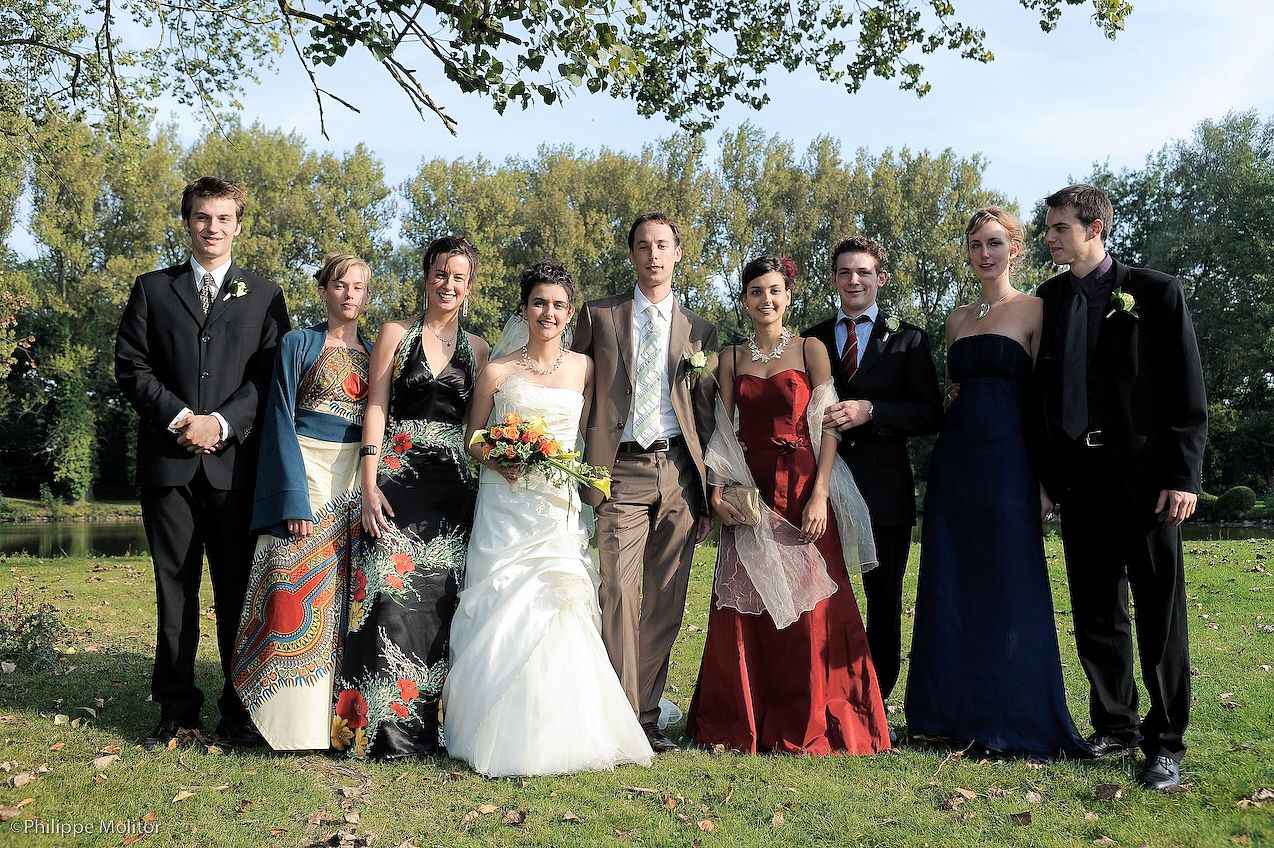 Wedding party posing outdoors in formal attire, bride in white gown with groom and bridesmaids in colorful dresses.