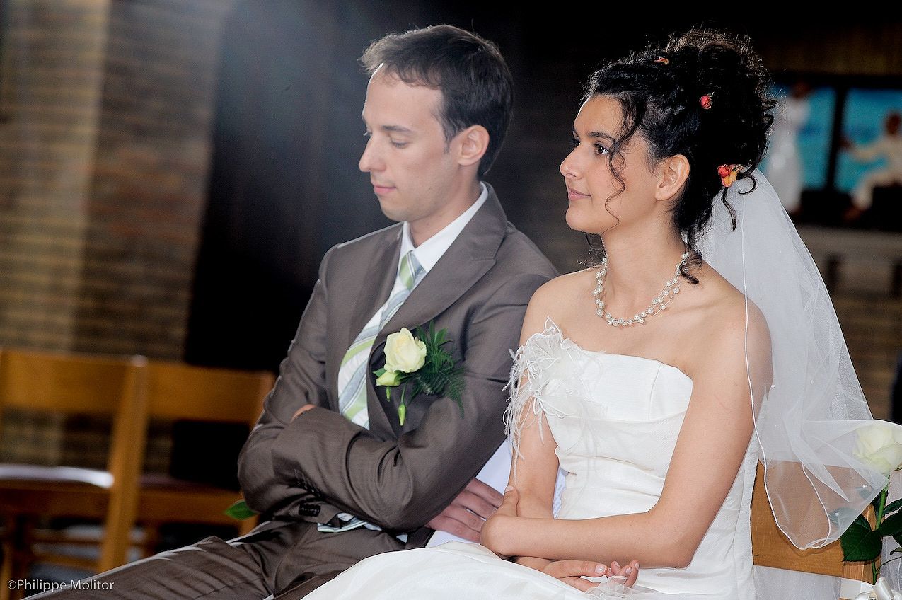 Bride and groom sitting together during wedding ceremony, bride in white dress with veil, groom in gray suit with white boutonniere.