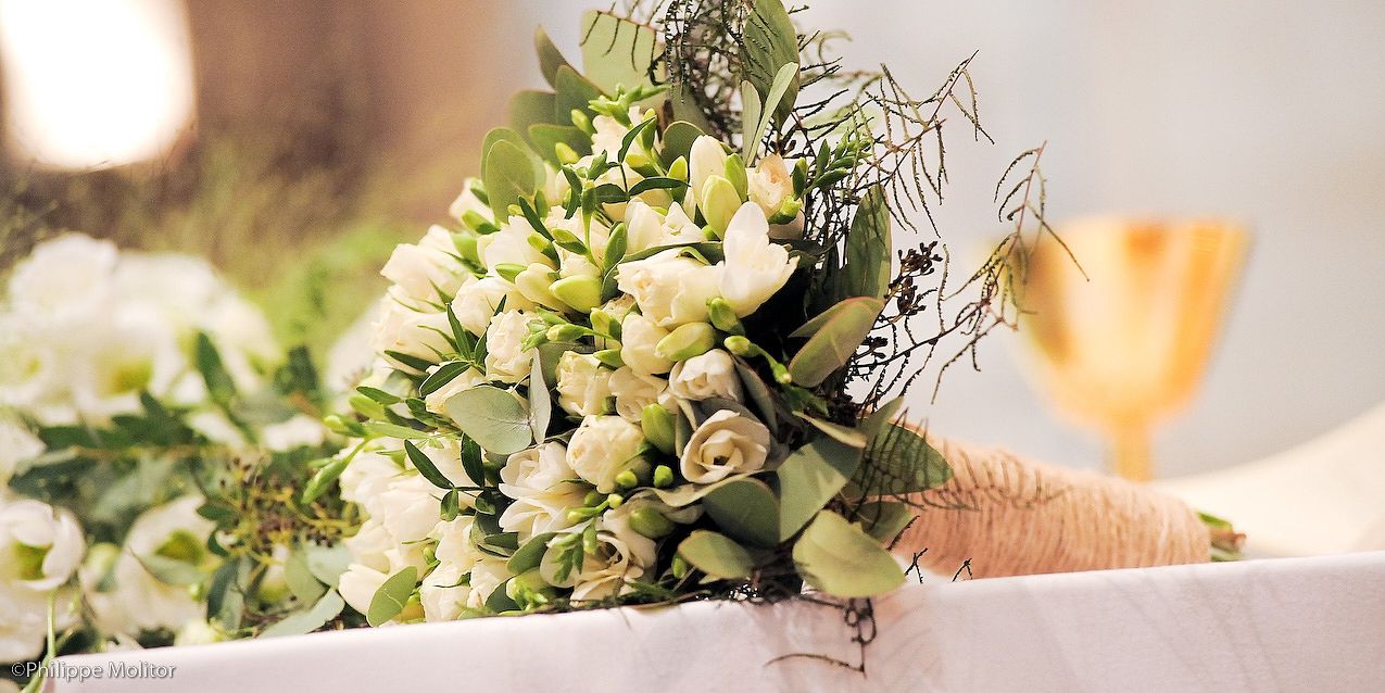 Elegant white wedding bouquet with roses and greenery on a table beside a champagne glass.