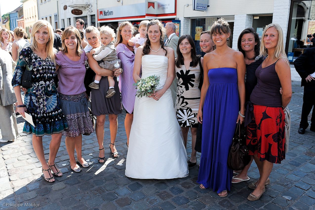 Bride in white gown poses with bridesmaids and female guests outdoors on a sunny wedding day.