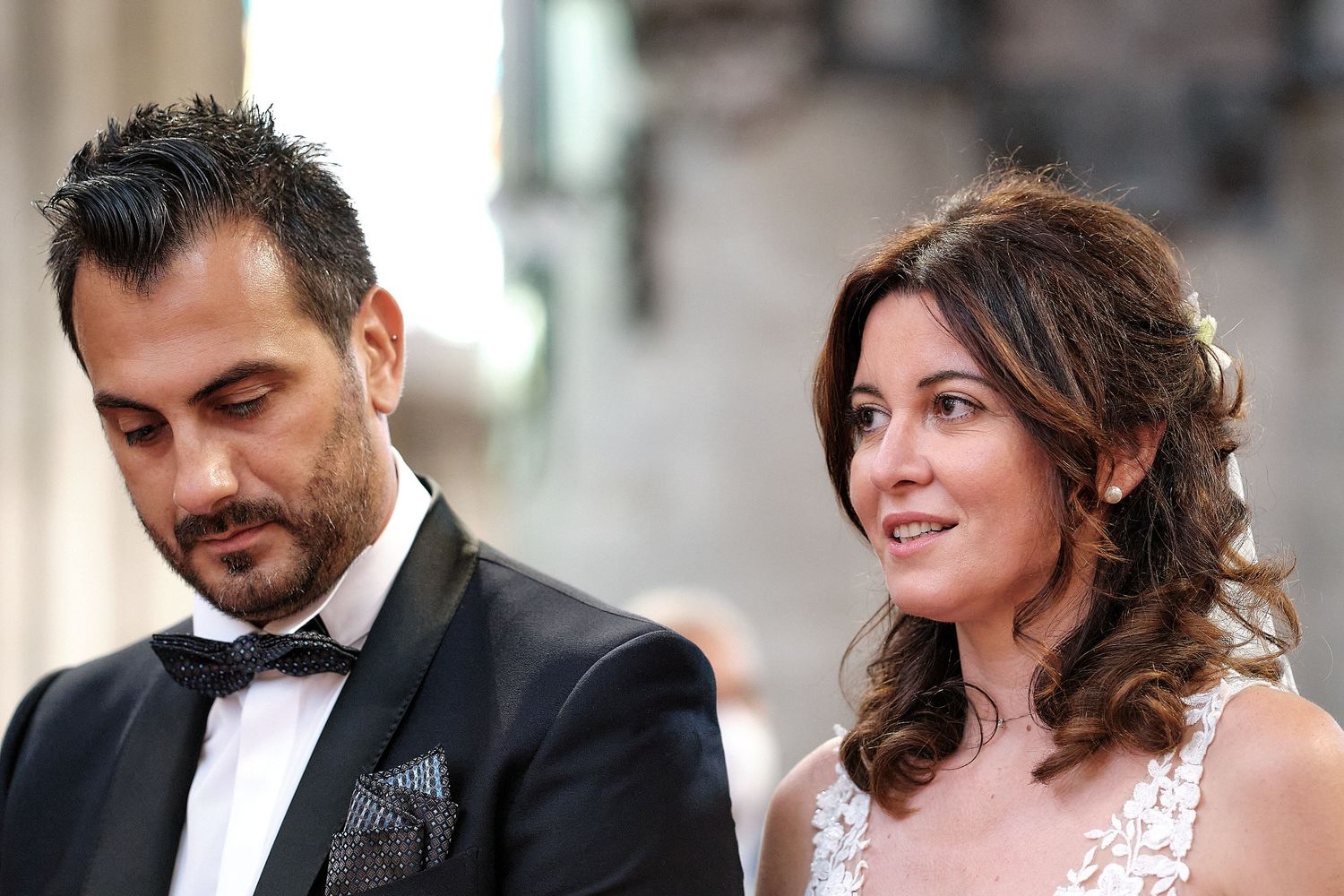 Elegant couple dressed in formal attire at a glamorous event, man in tuxedo and woman in white lace dress.