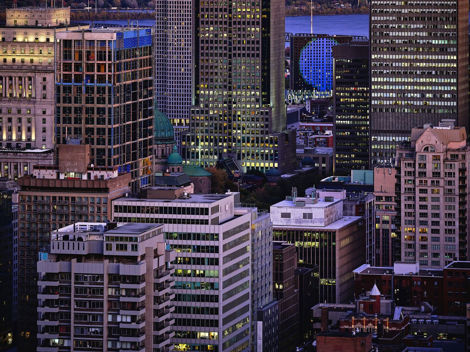 Urban skyline at dusk showing illuminated office buildings and skyscrapers.