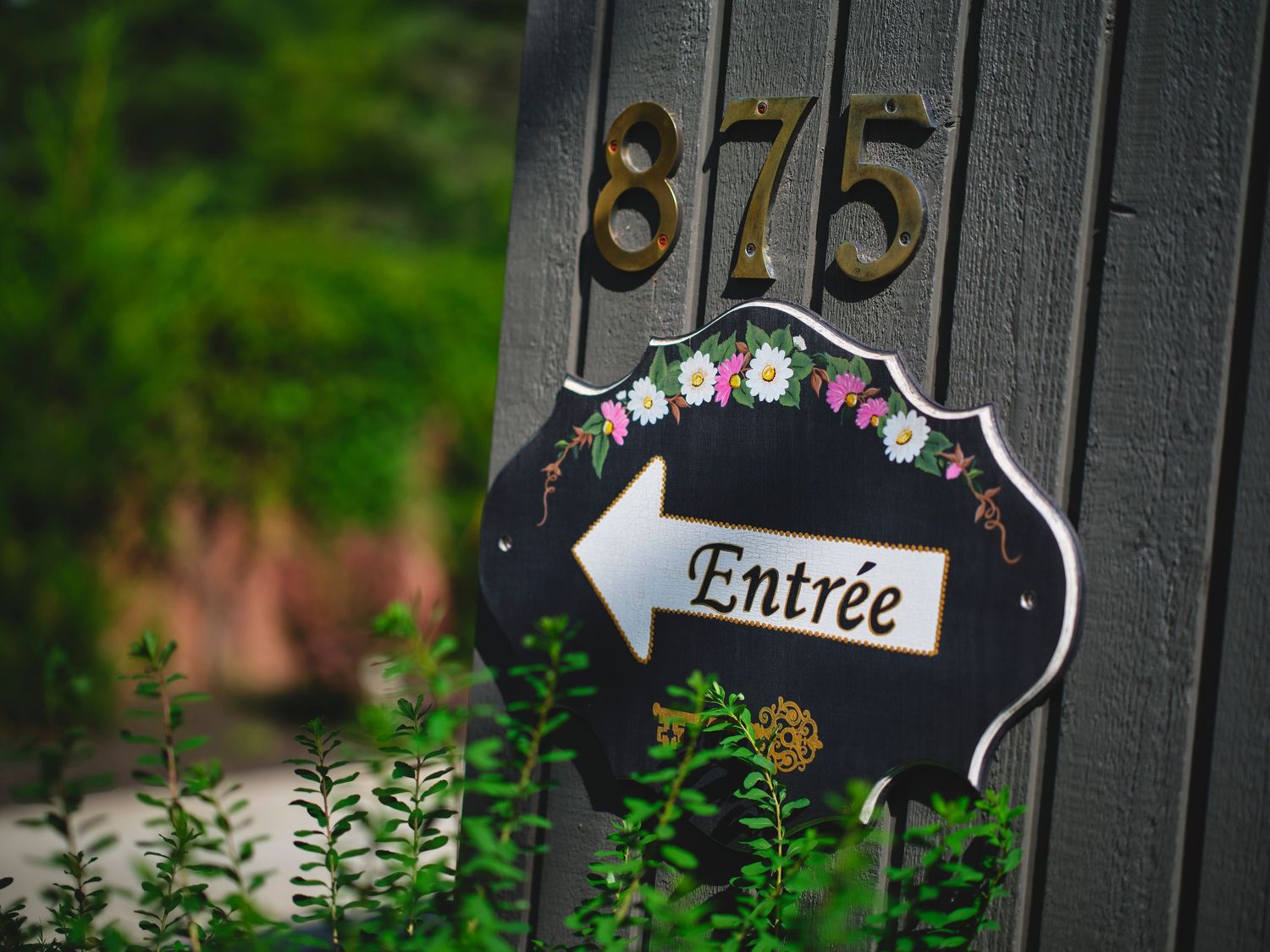 Black entrance gate with decorative signage and lush green foliage.