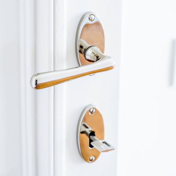 Modern door handle and lock mechanism in chrome and copper finish on white door.