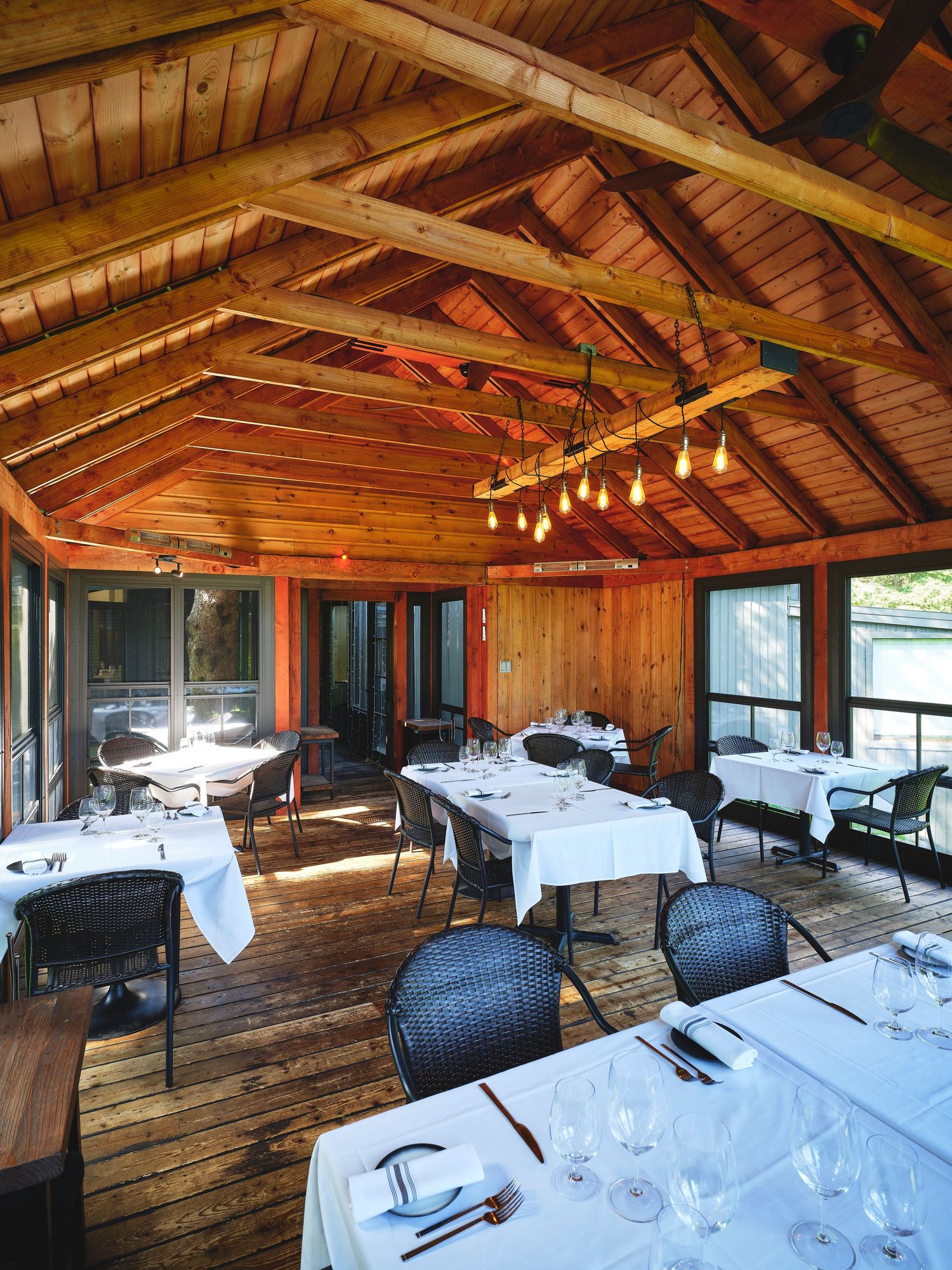 Rustic wooden dining room with exposed beam ceiling, pendant lights, and elegant table settings.