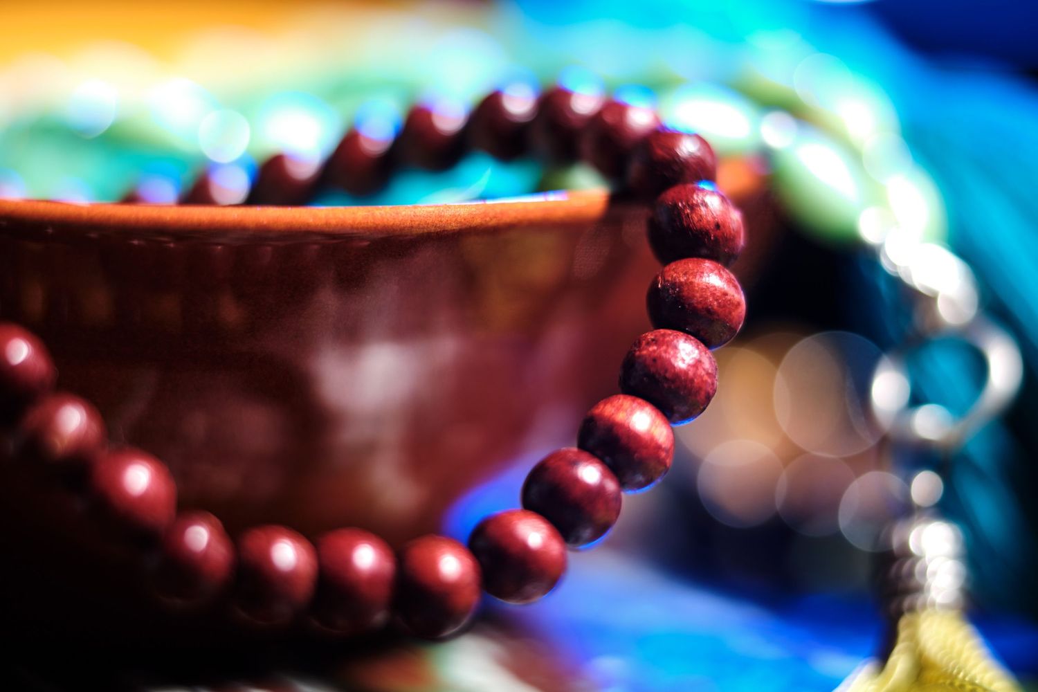 Red prayer beads or bracelet photographed with colorful bokeh lighting effects.