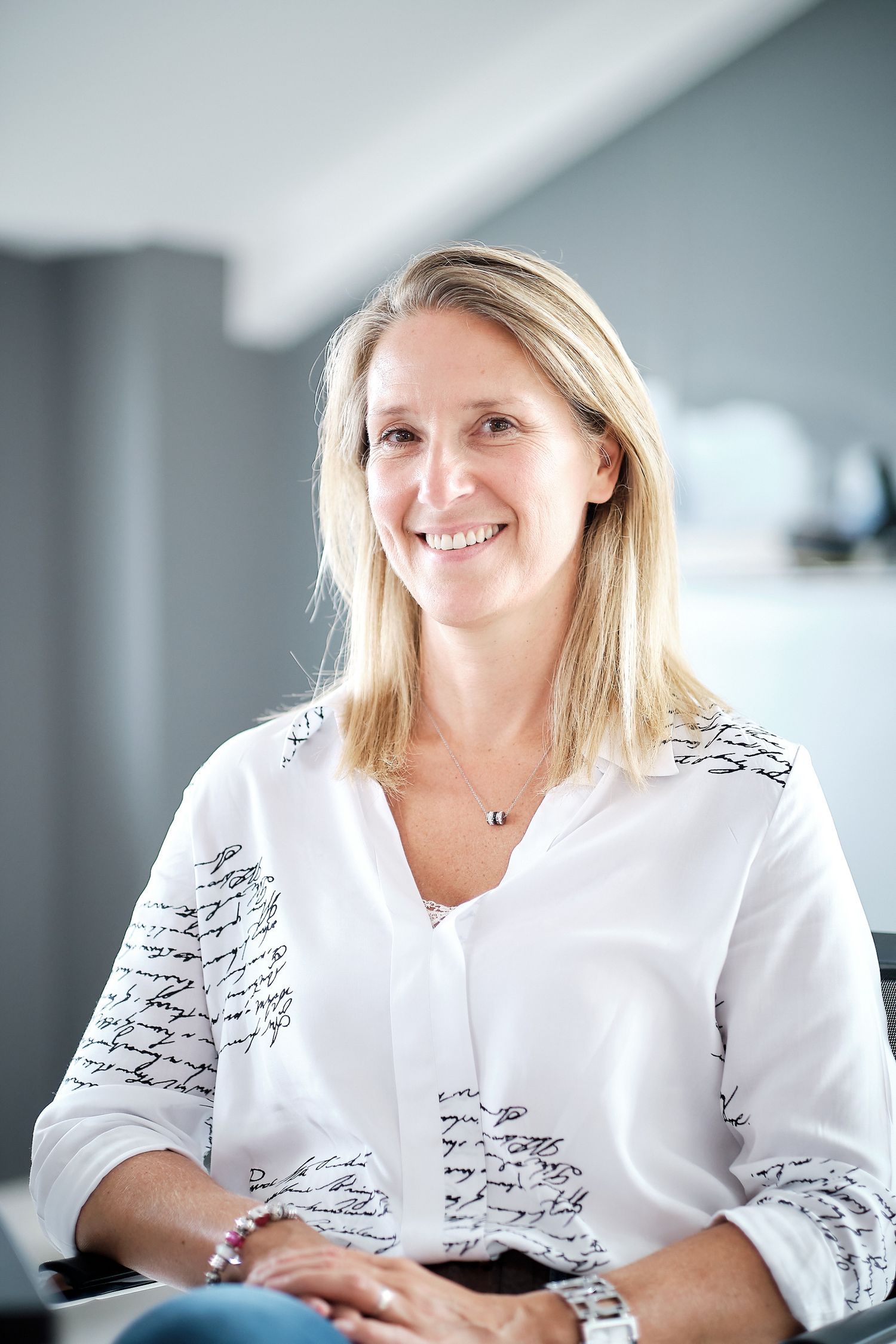 Professional portraits of person in white patterned blouse in bright office setting.