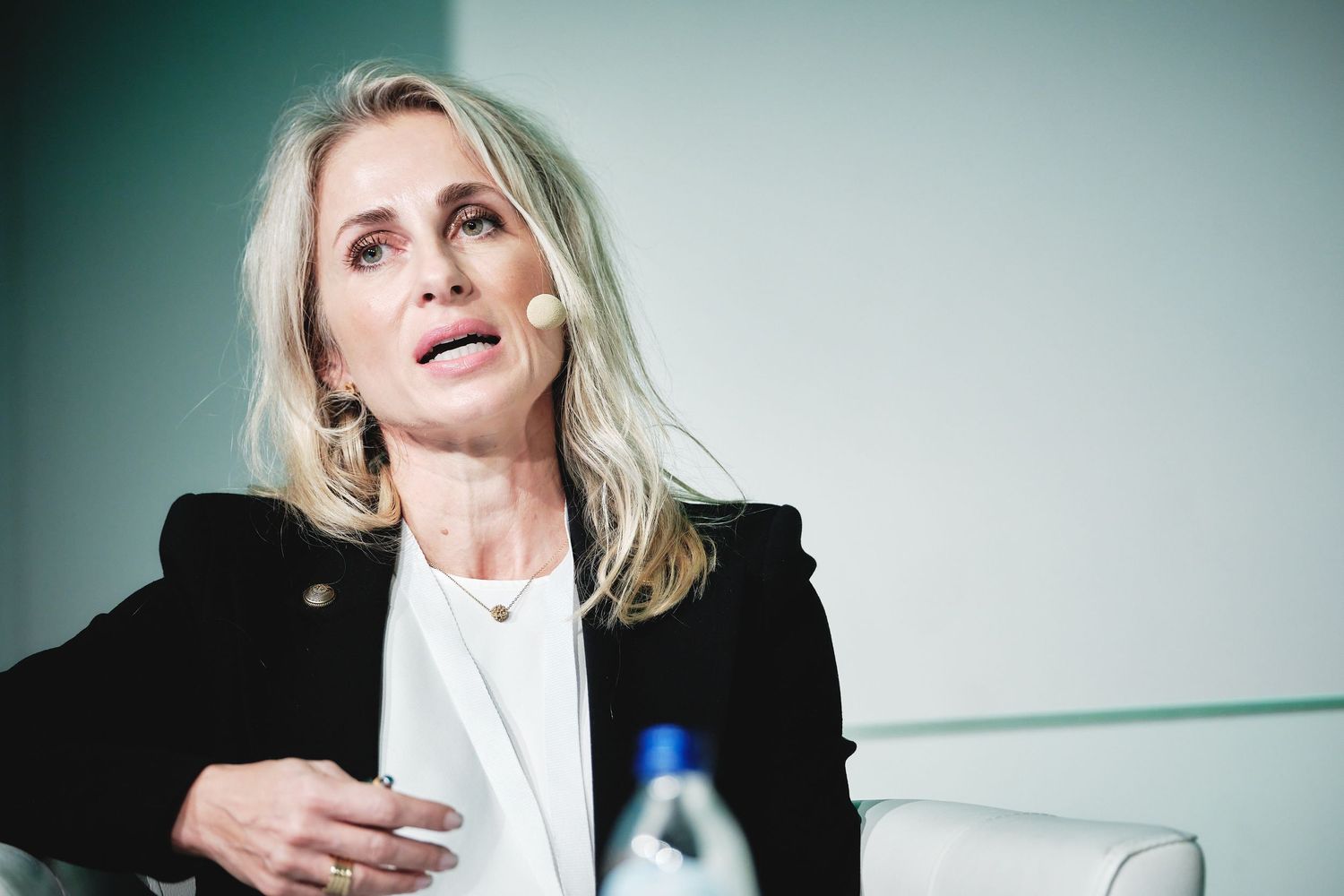 Professional speaker in black blazer and white top engaged in discussion at conference panel.