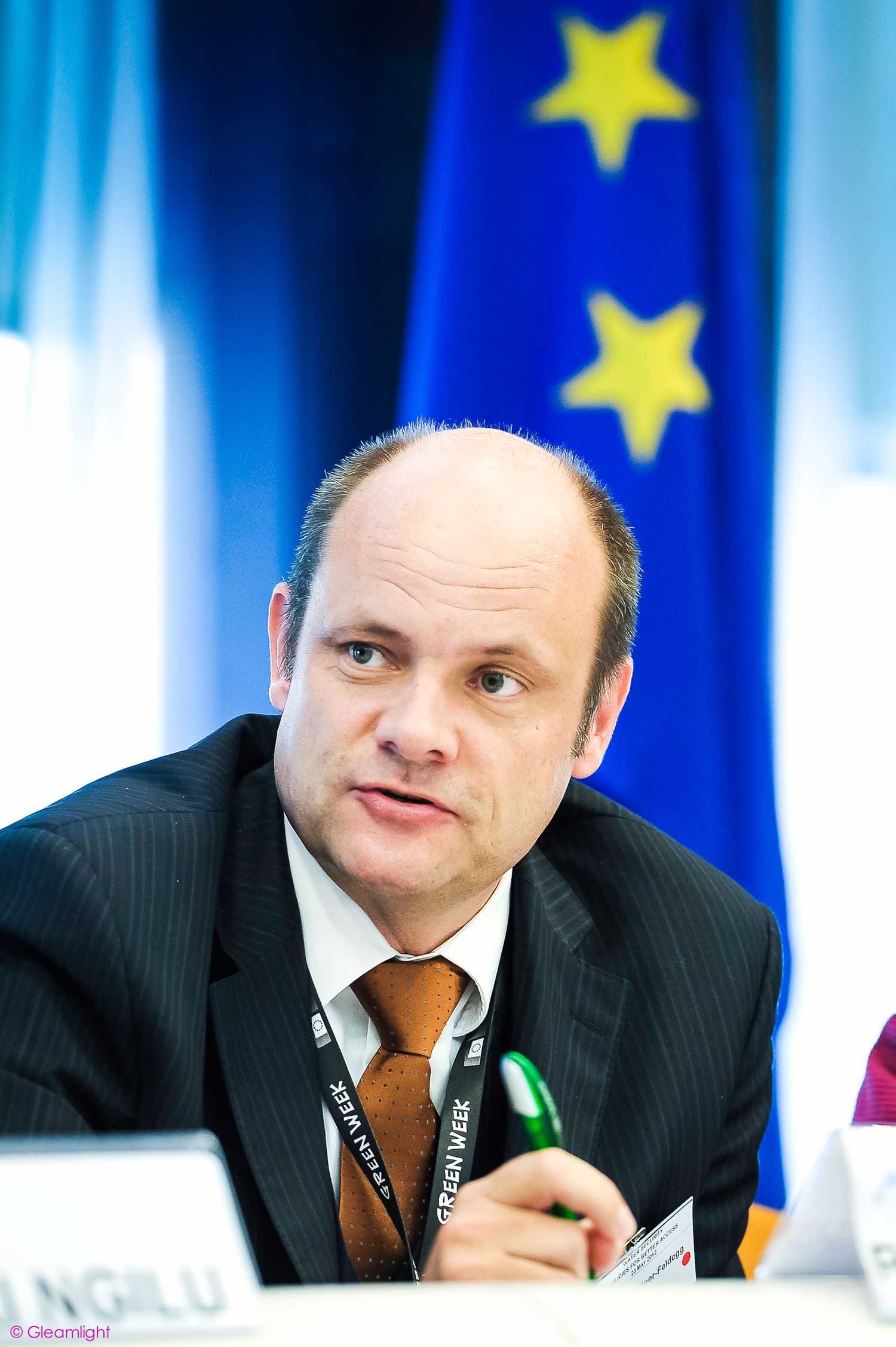 Speaker at European Parliament meeting with EU flag backdrop.