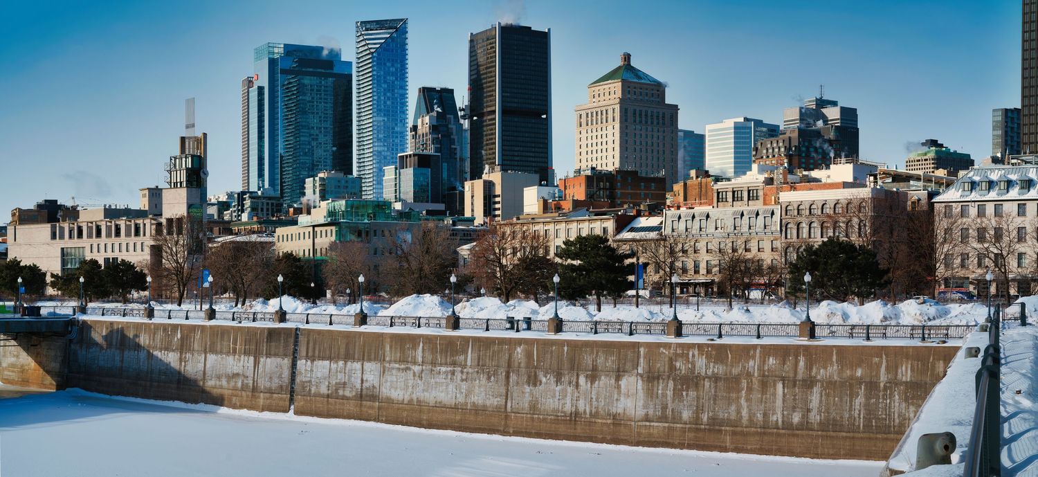 Panoramic cityscape view of Boston's skyline and waterfront with snow-covered ground on a clear winter day.