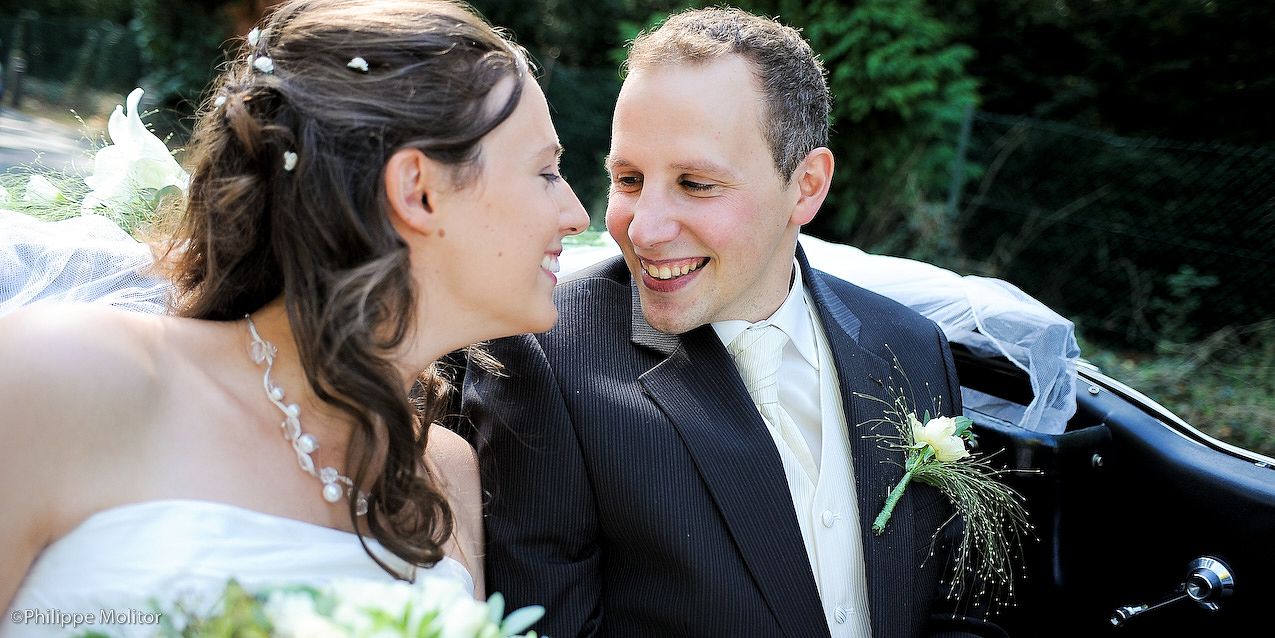 Happy bride and groom smiling at each other near a decorated car on their wedding day.