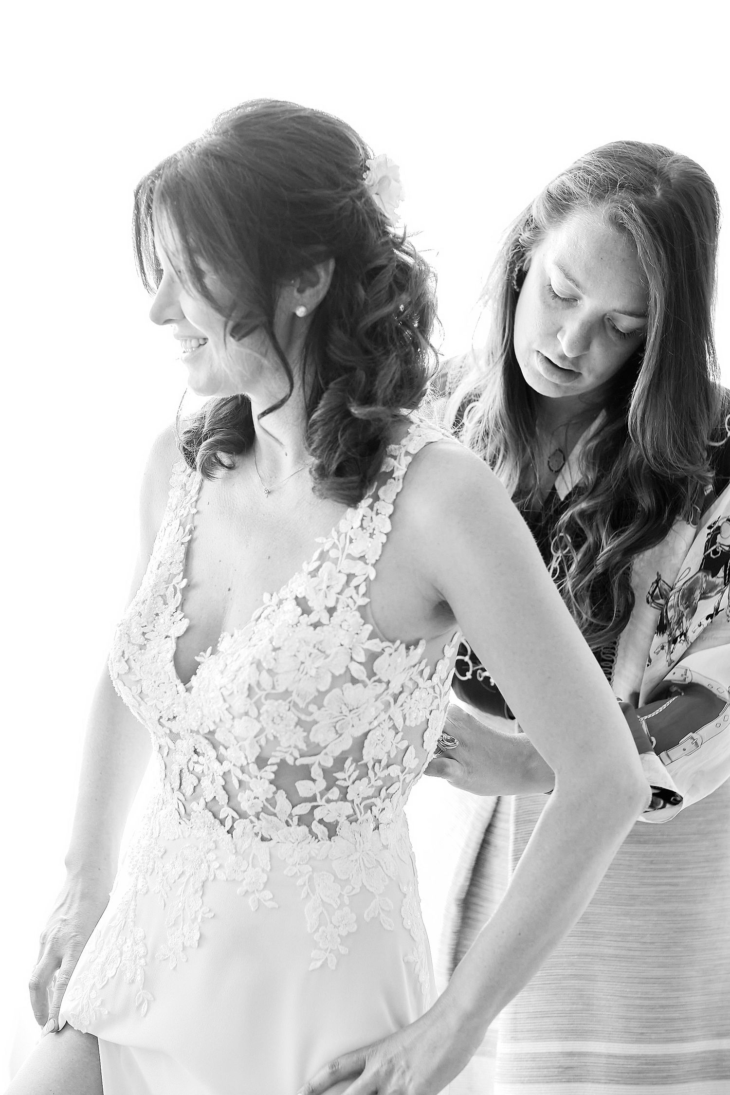 Bridesmaid helping bride with her lace wedding dress in elegant black and white bridal preparation photo.