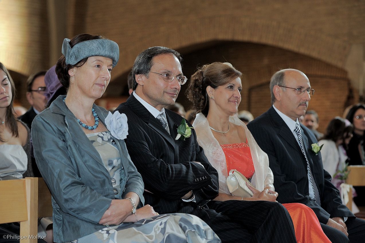 Four elegantly dressed wedding guests seated in a church, smiling during a wedding ceremony.