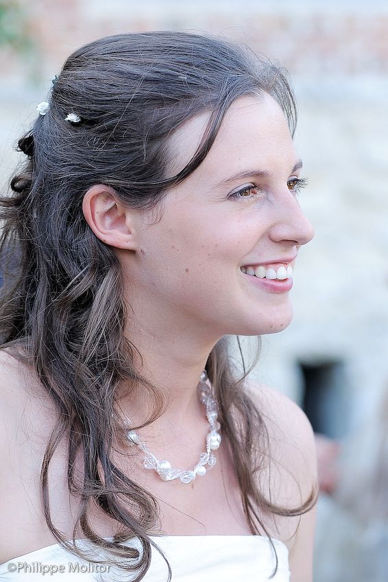 A smiling bride in profile view wearing a pearl necklace and white dress with hair accessories.