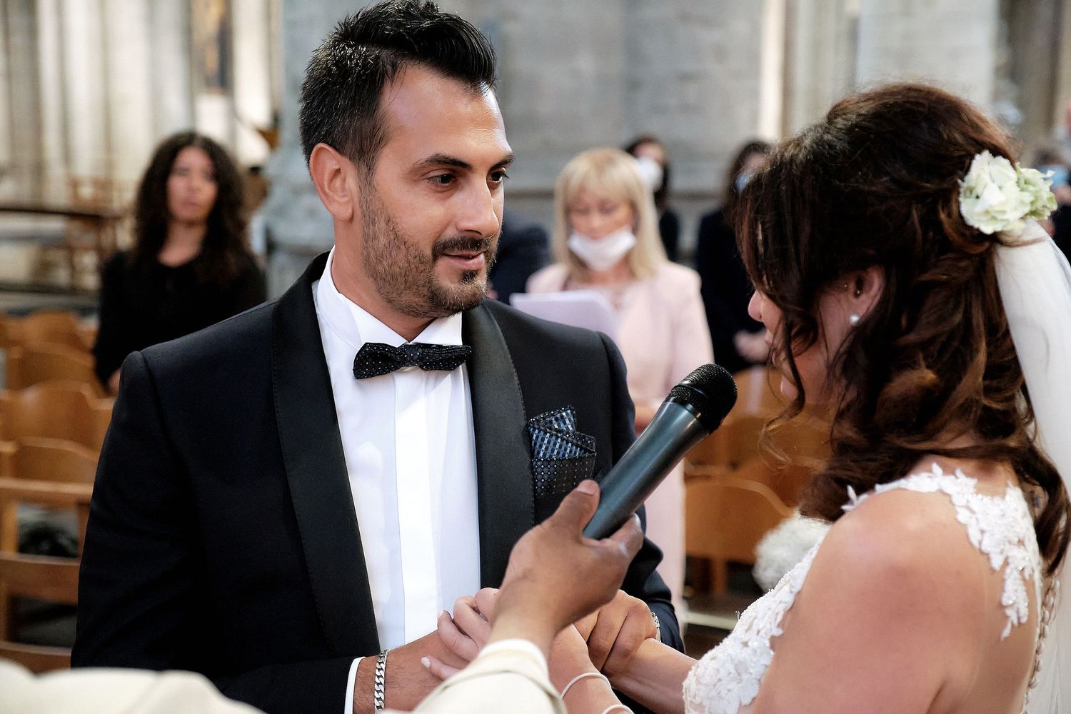 Groom in tuxedo exchanging vows with bride holding microphone during elegant church wedding ceremony.
