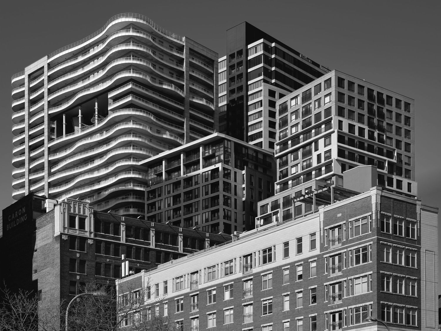 Black and white photo of modern high-rise buildings with curved facades towering over older brick apartments in an urban cityscape.