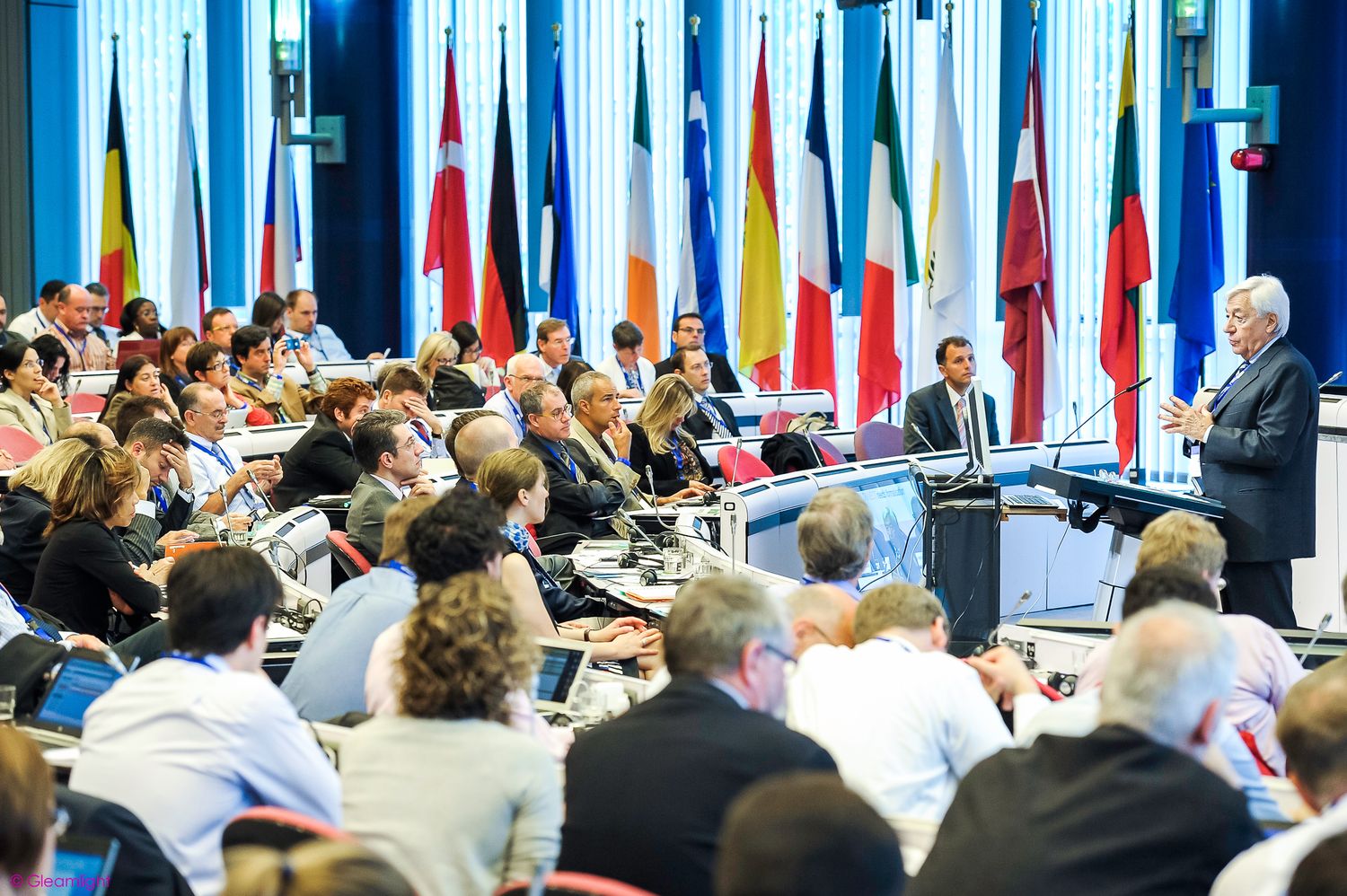 Wide view of conference room filled with attendees and international flags on display.