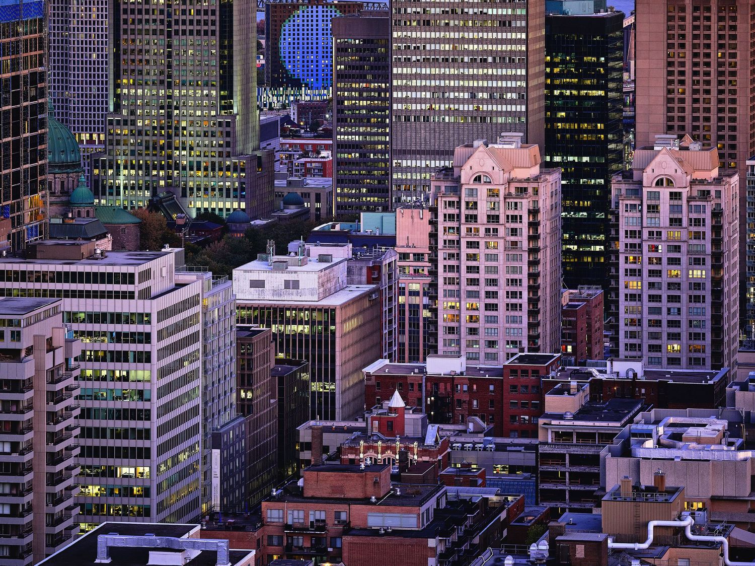 City buildings and skyscrapers lit up against a purple twilight sky.