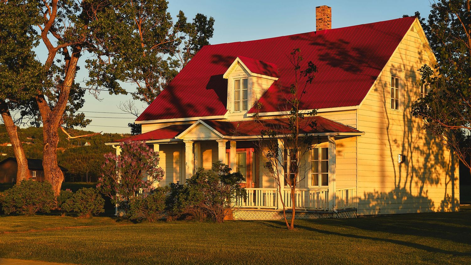 Row of red-roofed yellow farmhouses nestled among autumn trees at sunset.