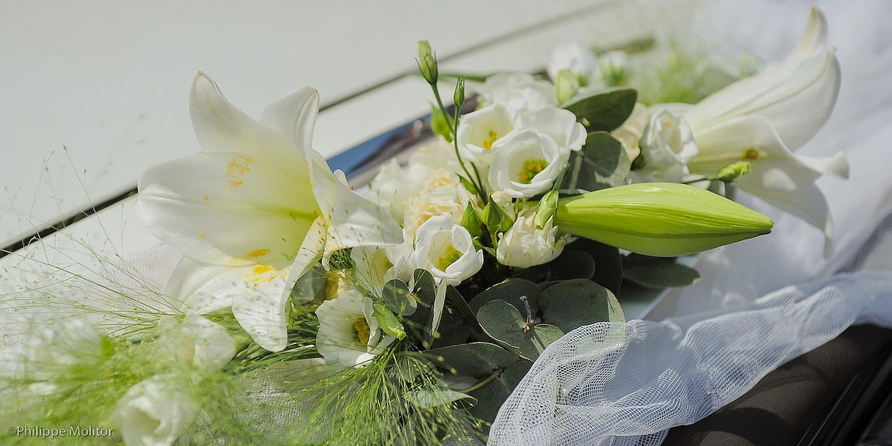 Elegant white wedding bouquet featuring lilies and roses with green foliage on a white surface.