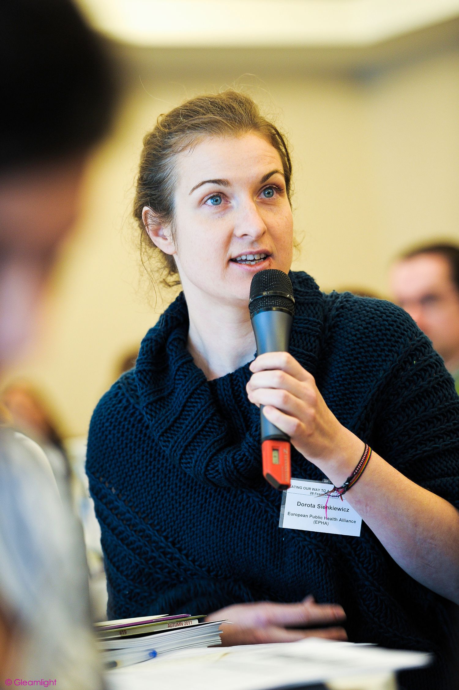 Attendee in navy sweater speaking into microphone during conference session.