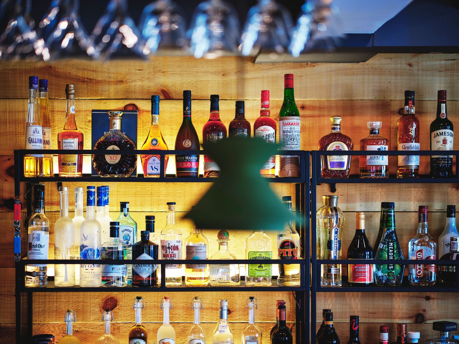 Illuminated bar shelf displaying various spirits and liquor bottles against wooden backdrop.