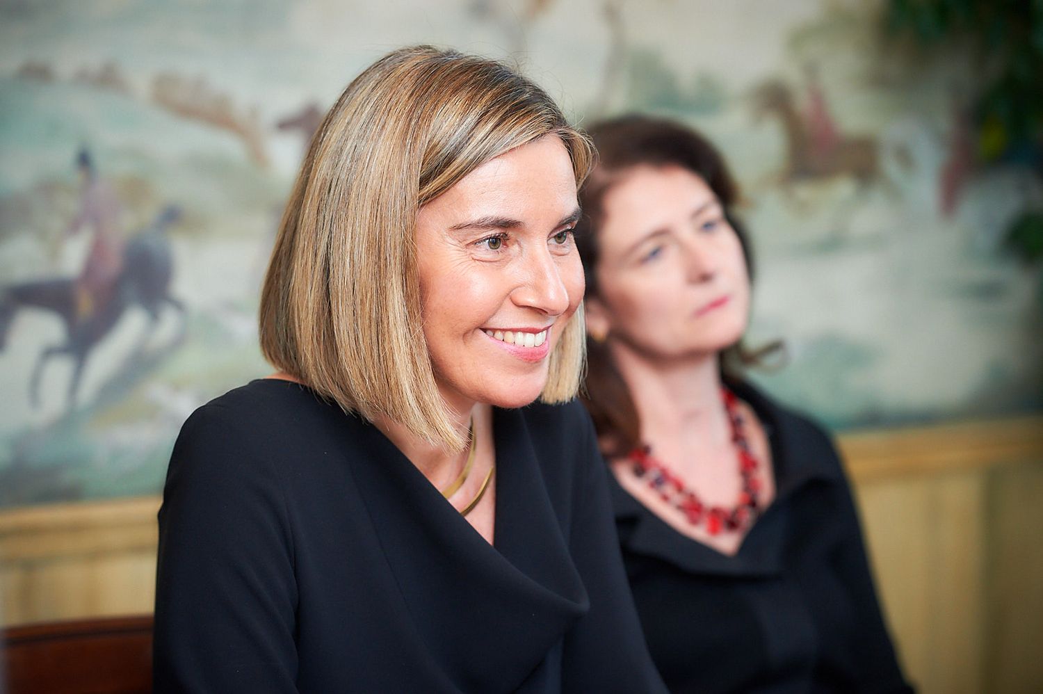 Two people in professional attire are captured in conversation with a decorative wall mural behind them.