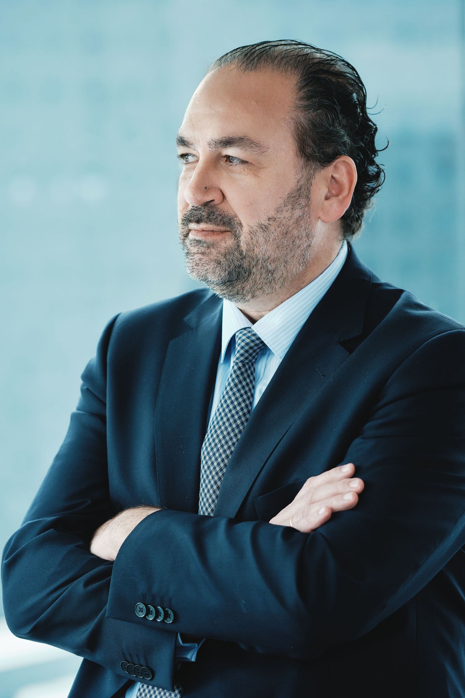 Business portrait of executive in navy suit with crossed arms against modern backdrop.