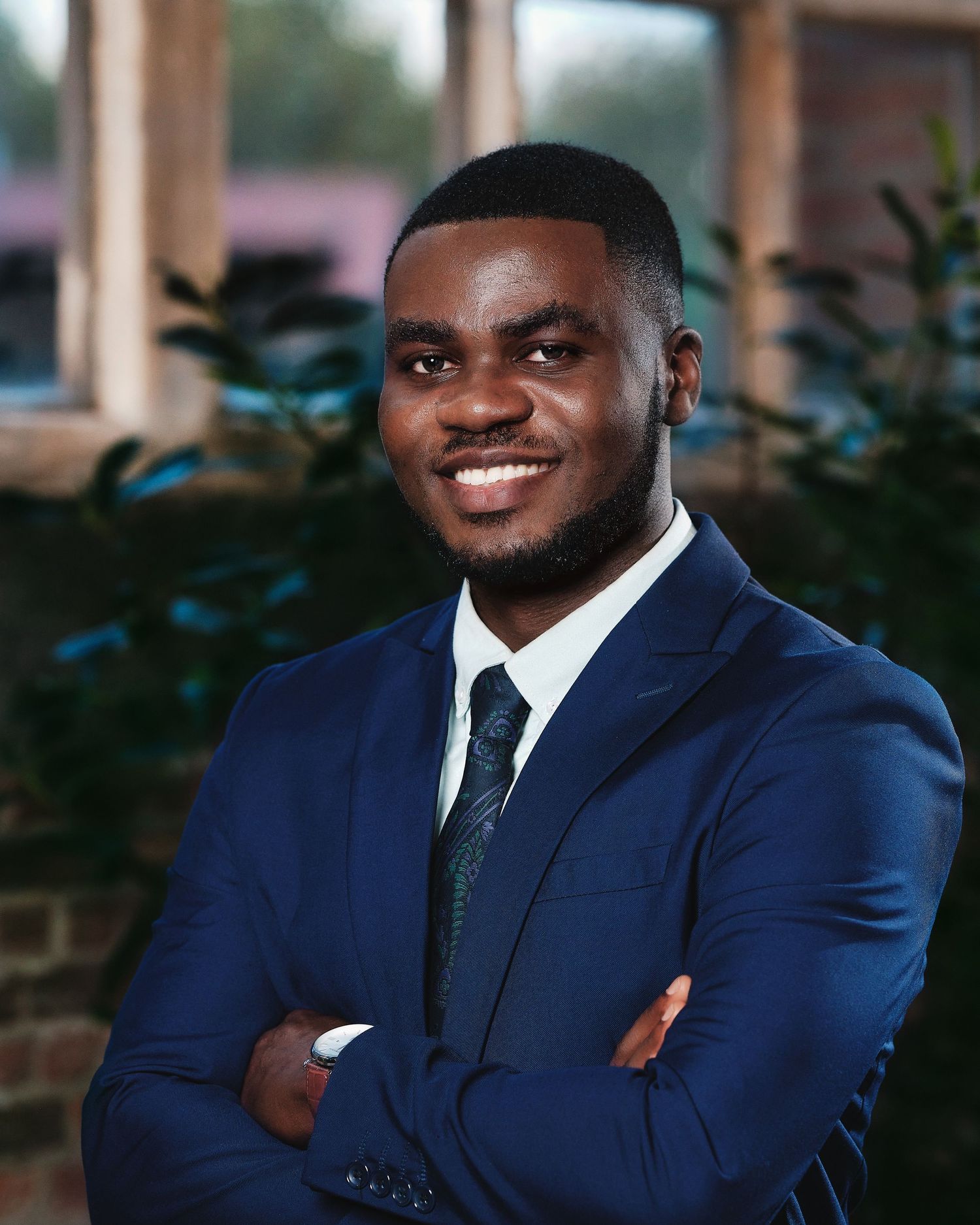 Professional in navy suit and tie smiles confidently in office setting.