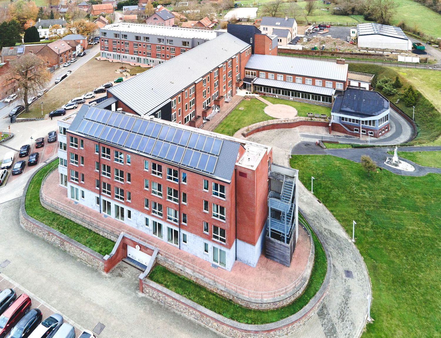 Modern red brick educational building with solar panels on roof captured in aerial view.