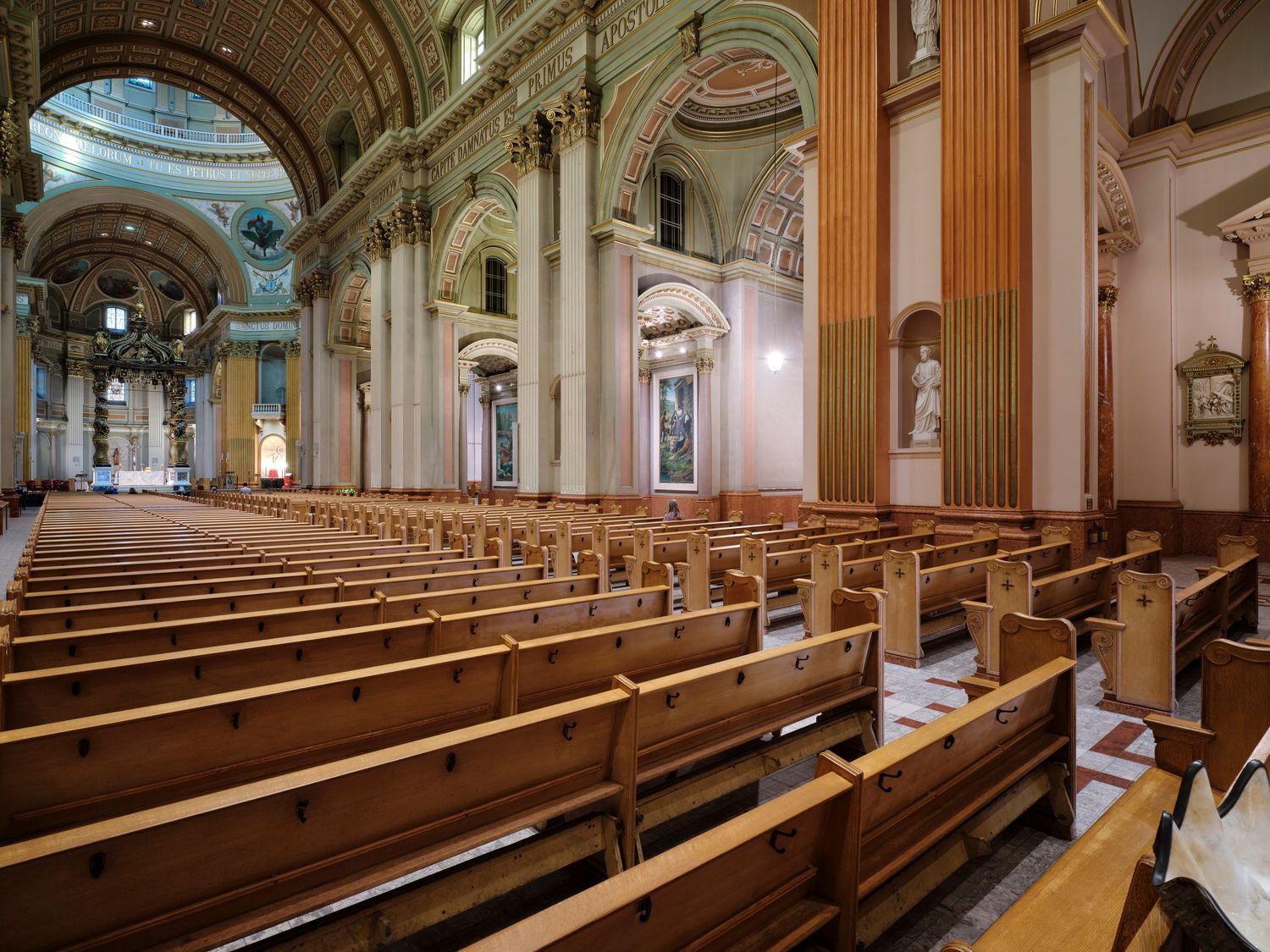 Grand cathedral interior with rows of wooden pews, ornate columns, arched ceilings, and classical architecture.