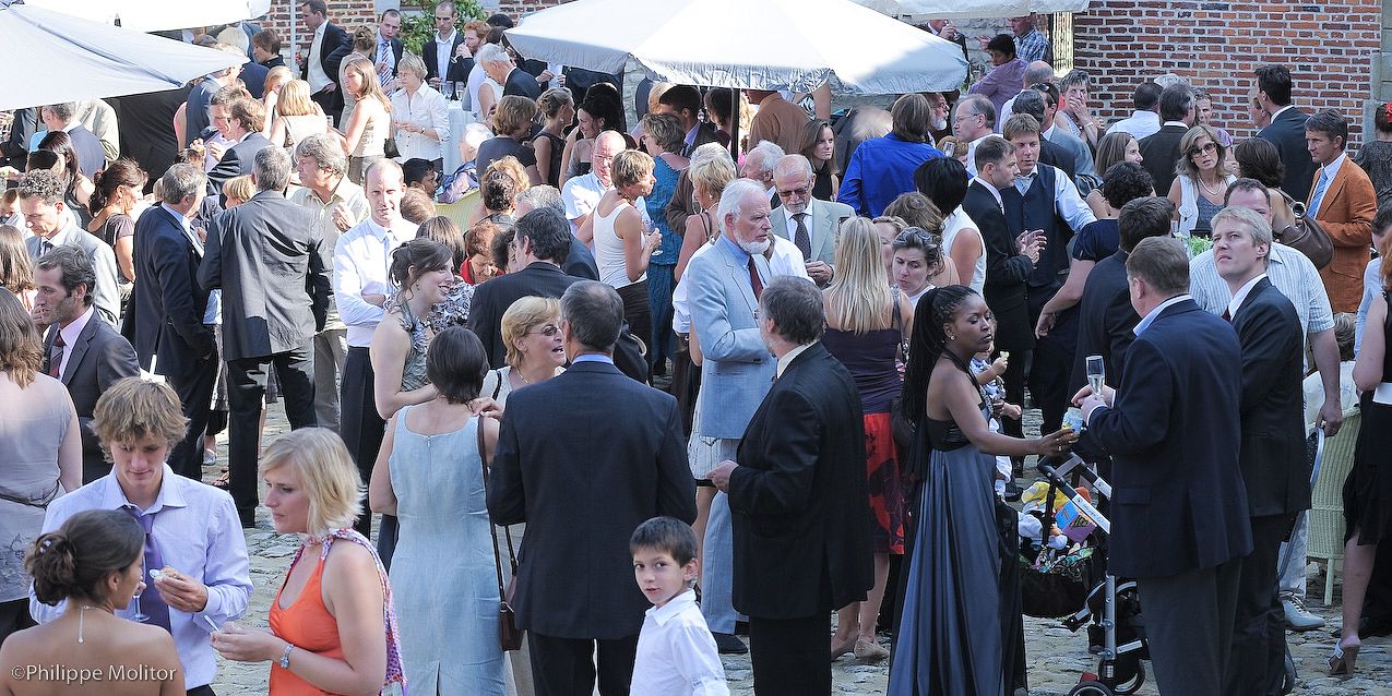 Elegant outdoor wedding reception with guests mingling in formal attire on a sunny day.