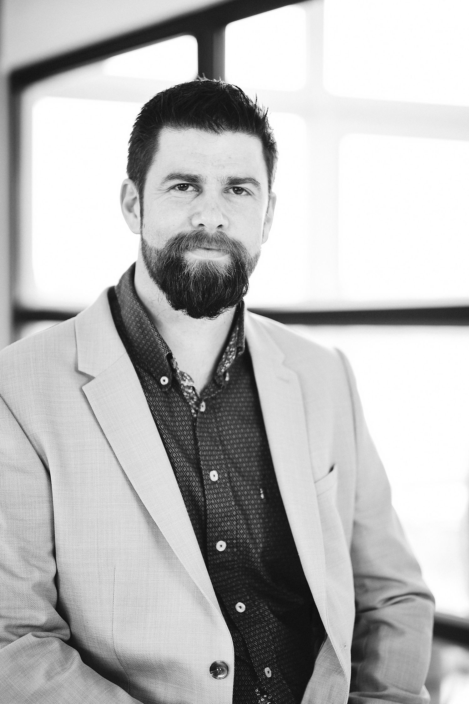 Professional portrait series showing light gray suit and dark shirt against bright office background.