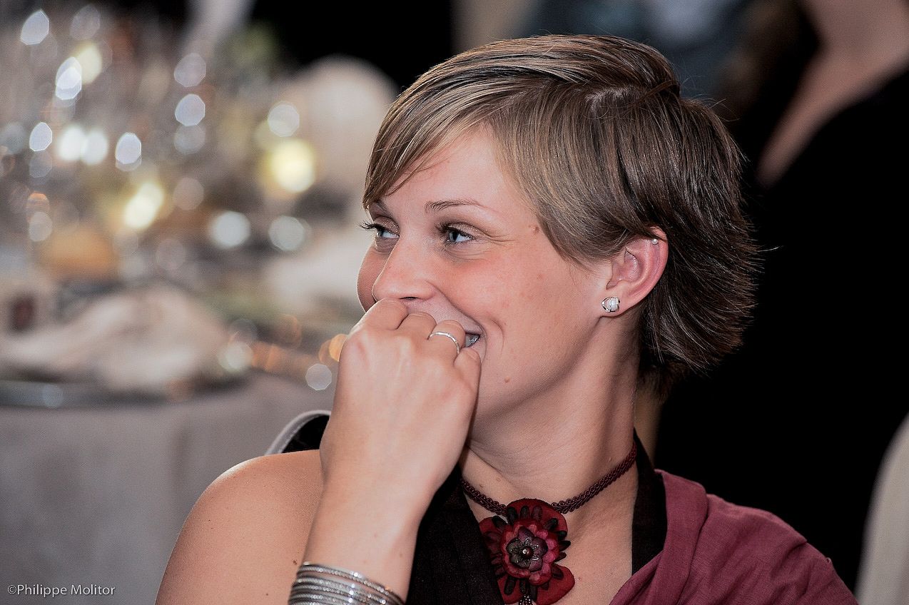 Smiling woman with short hair wearing a red flower necklace and silver bracelet at a formal dinner event.