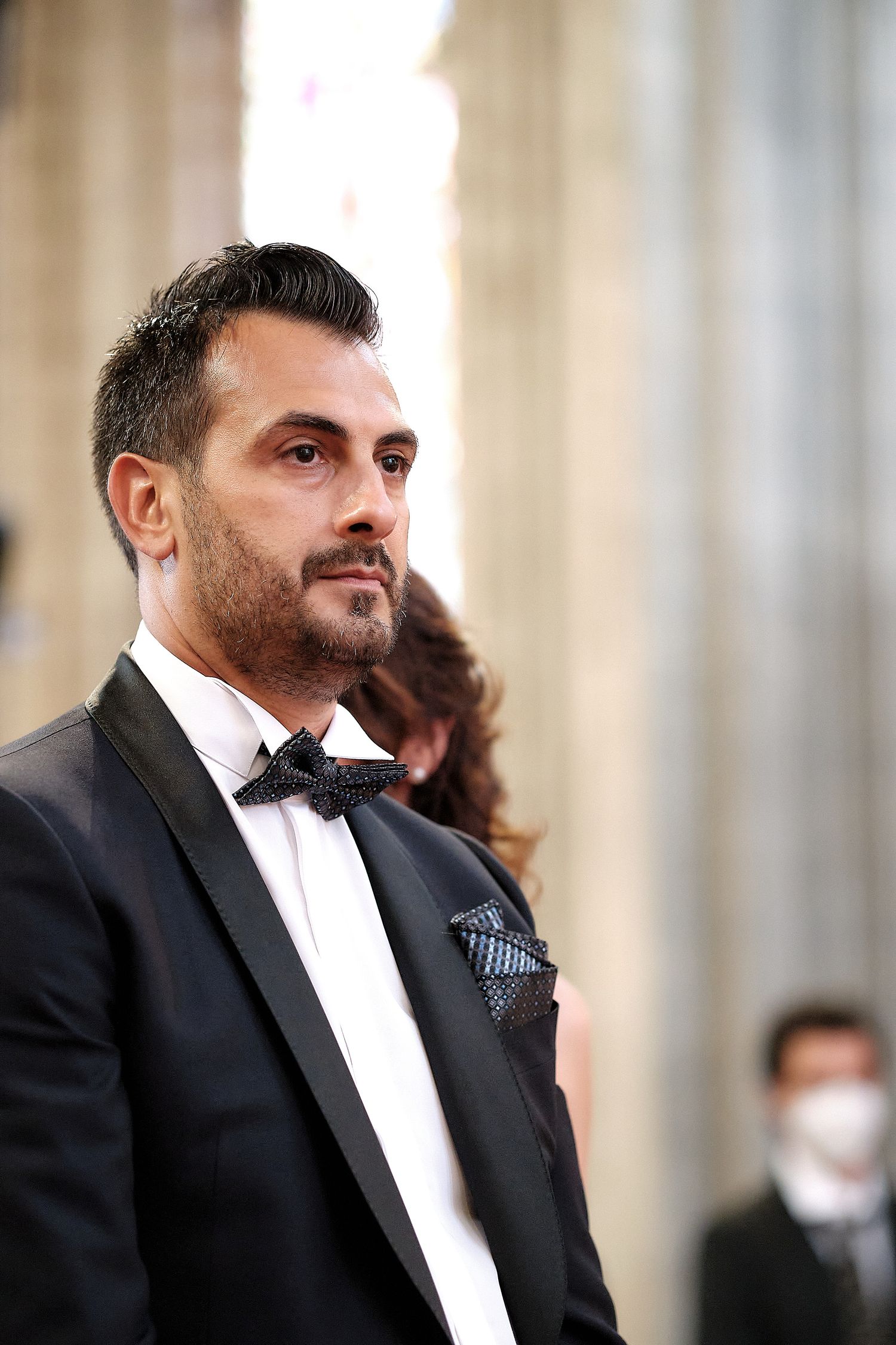Elegant man in black tuxedo with bow tie and pocket square at formal event.