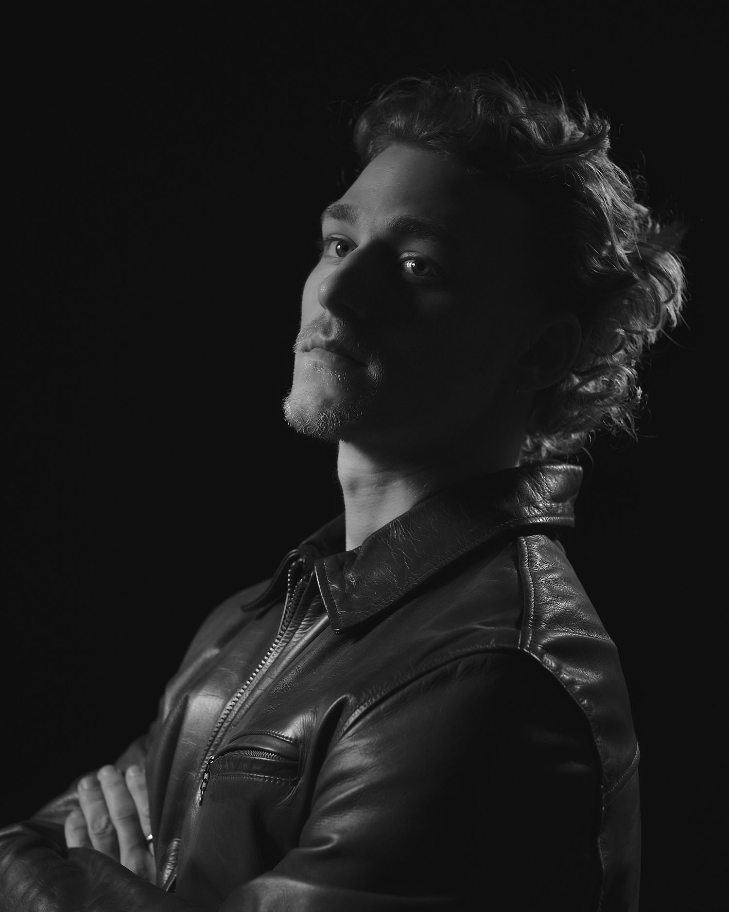 Person in leather jacket photographed against dark background with dramatic lighting.