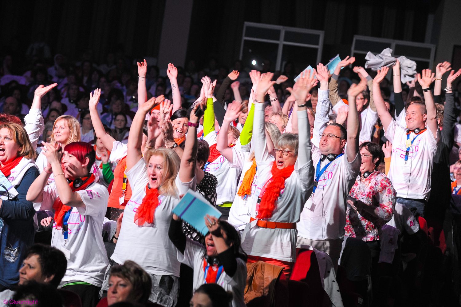 Large crowd with raised arms wearing white and red clothing at an event.