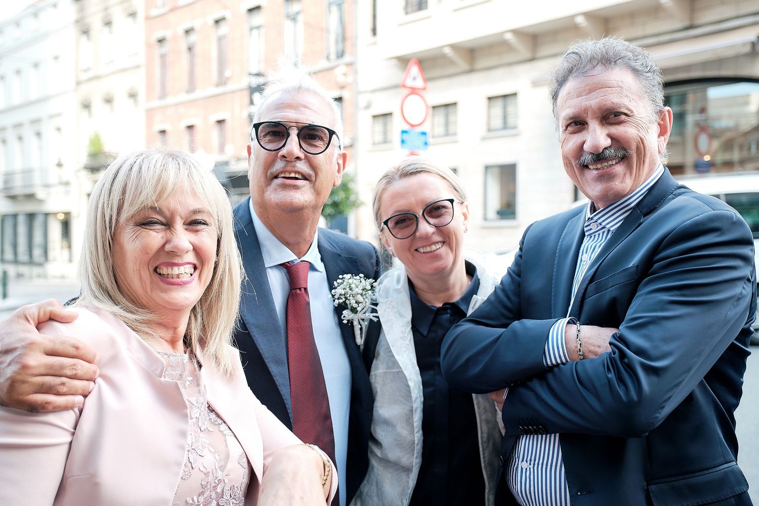 Four smiling adults posing together outdoors on a city street, dressed in formal attire for a special occasion.